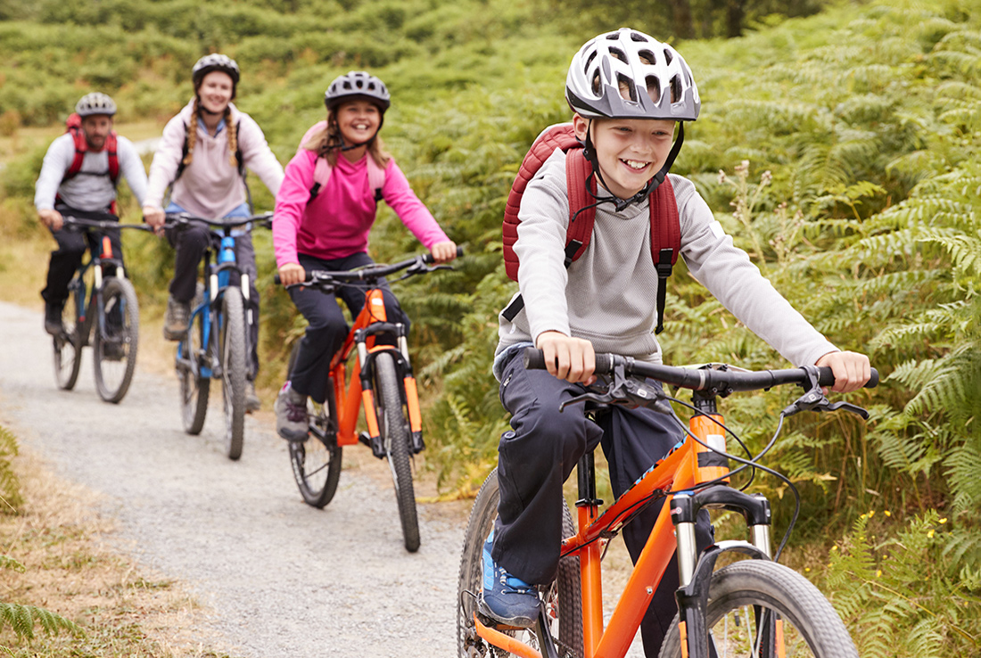 A family of four bike a trail wearing helmets.