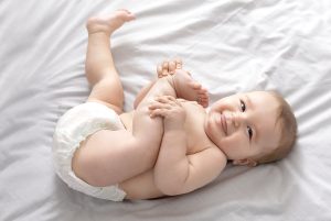 Happy baby in diaper laying on bed