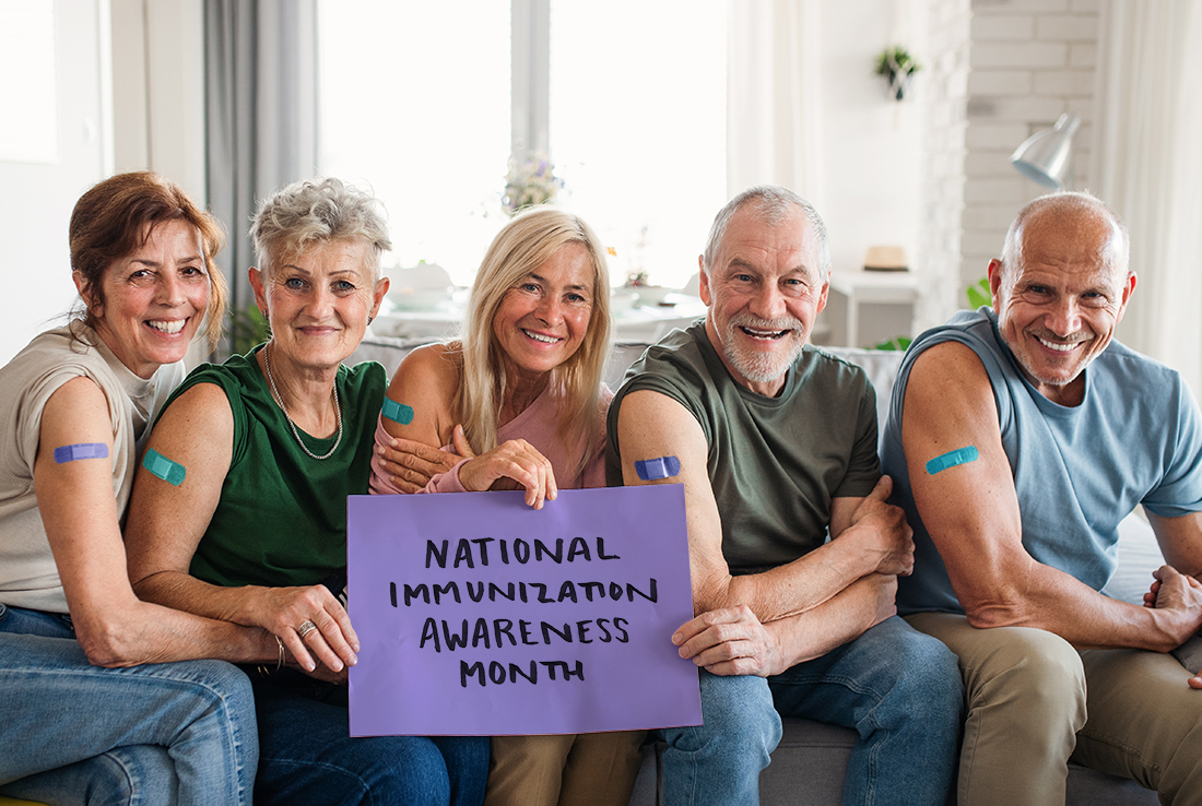 A group of senior citizens with bandaids on arms hold a sign reading "National Immunization Awareness Month".