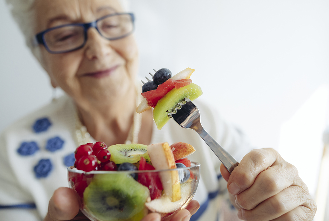 Older woman with gray hair and glasses eating a fruit salad with a fork
