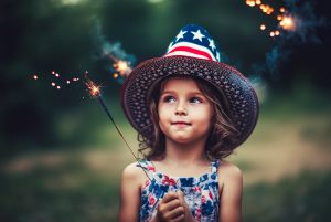 A little girl wearing a spangled hat holds a sparkler