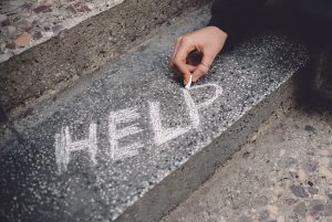 A teen's hand writing "HELP" in chalk on a sidewalk