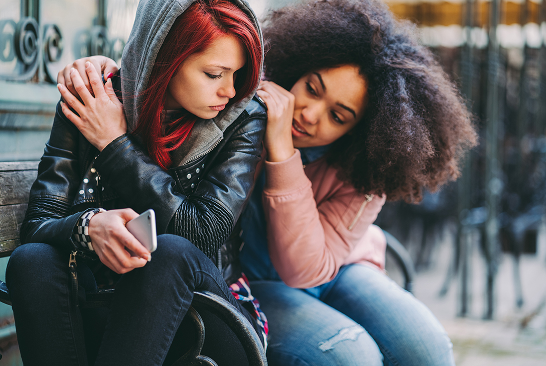 Two teenagers hugging and looking sad