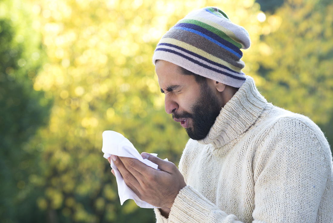 Man in hat sneezing into tissue.