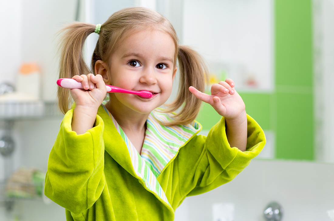 A little girl in pigtails and a bathroom brushes her teeth