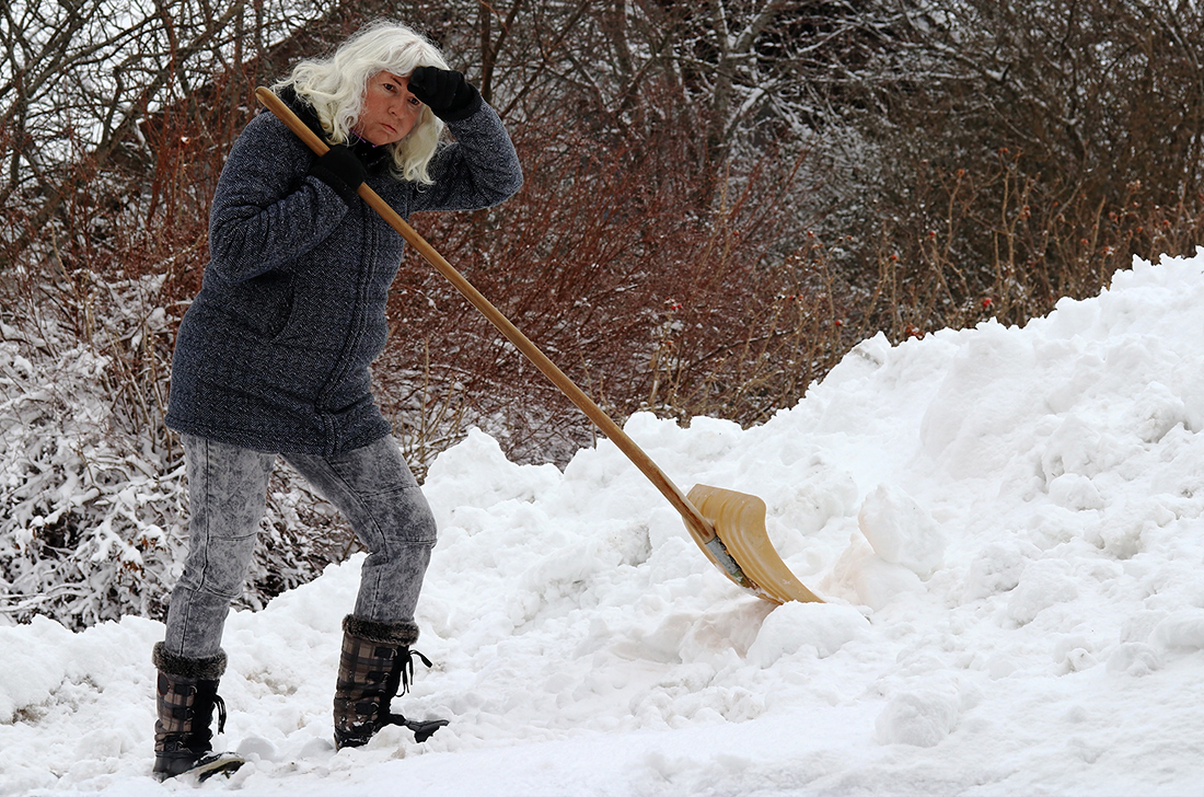 A senior in winter gear shovels snow